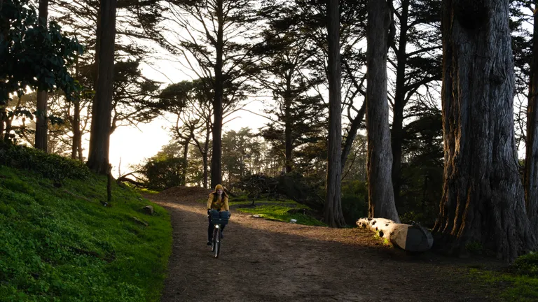 Kat riding down a dirt trail on Strawberry Hill with the sunset behind her highlighting a portion of the trail behind her.