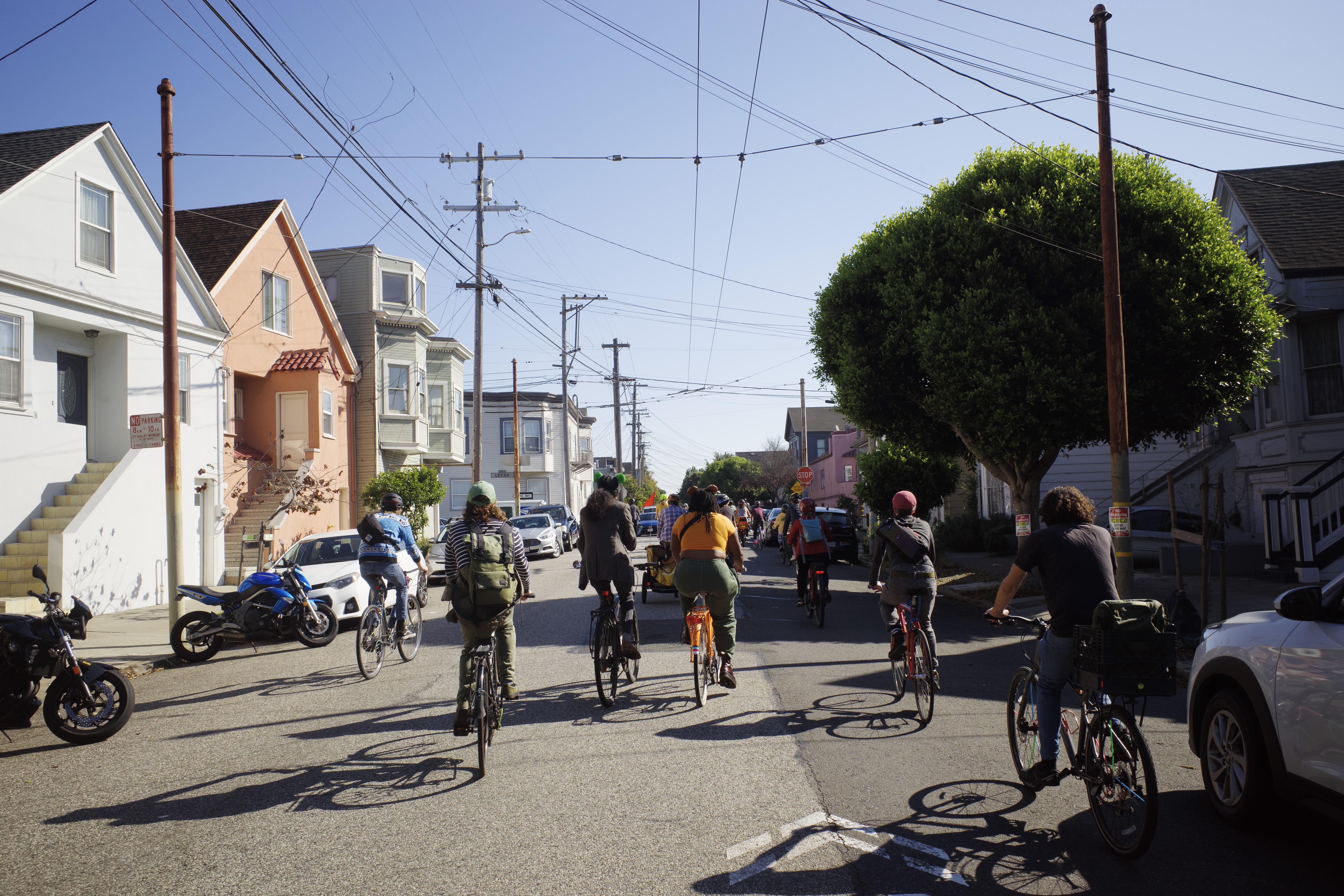 A group of cyclists in the sun going up a hill with lots of wires overhead