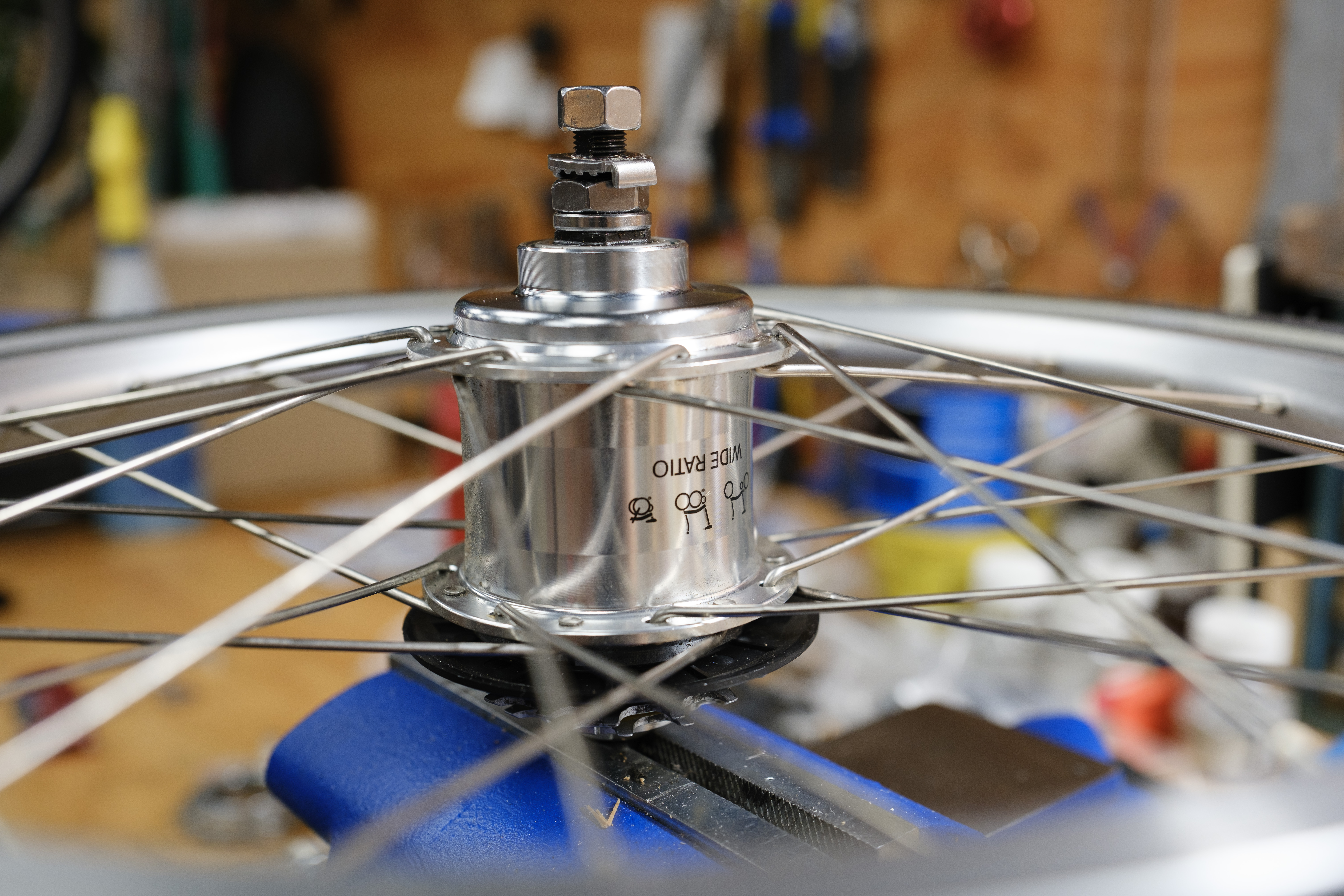 A Brompton rear wheel in a bench vise. The hub says 'Wide Ratio' with the Brompton folding logo.
