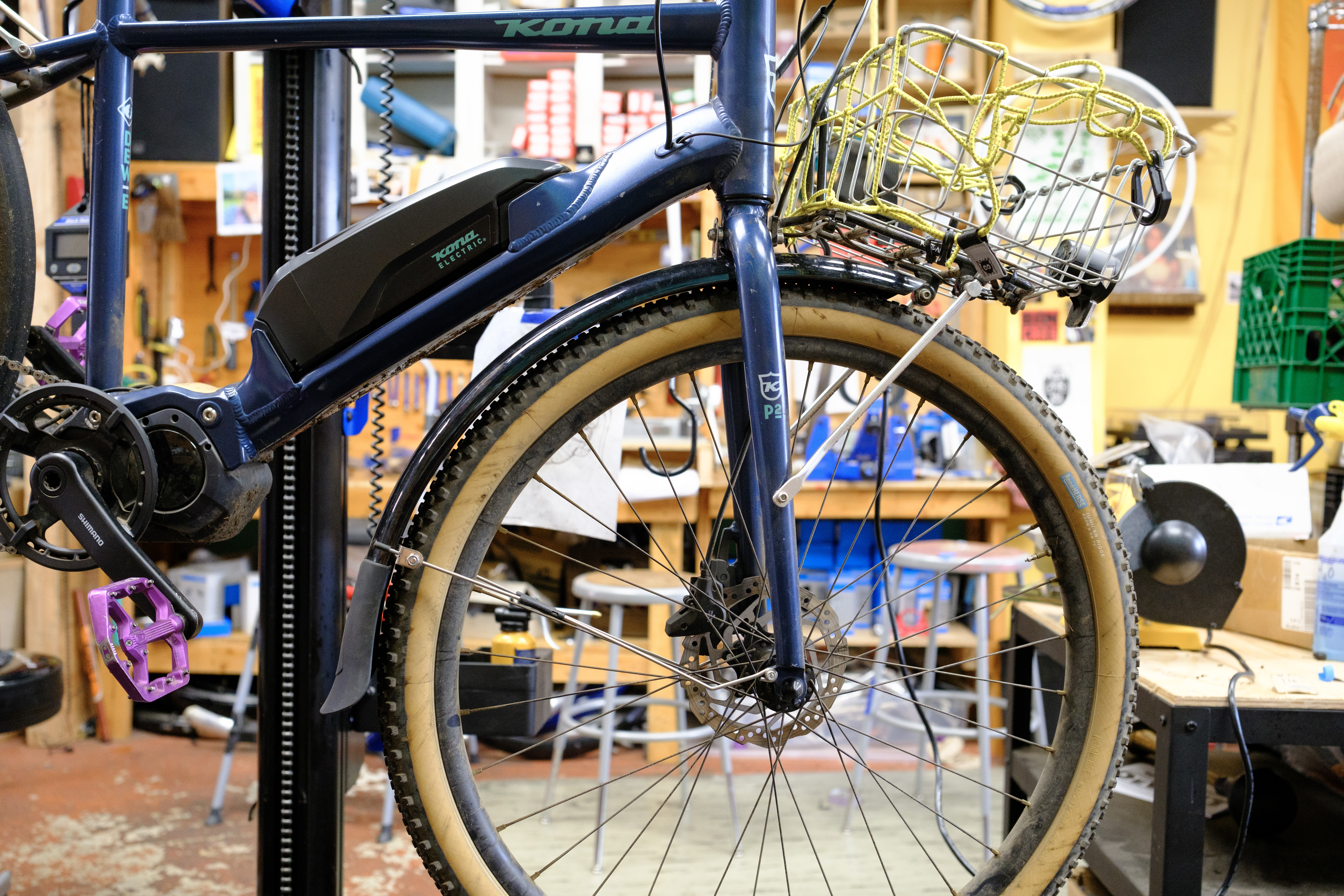 The front of a blue bike with a silver basket and black fender