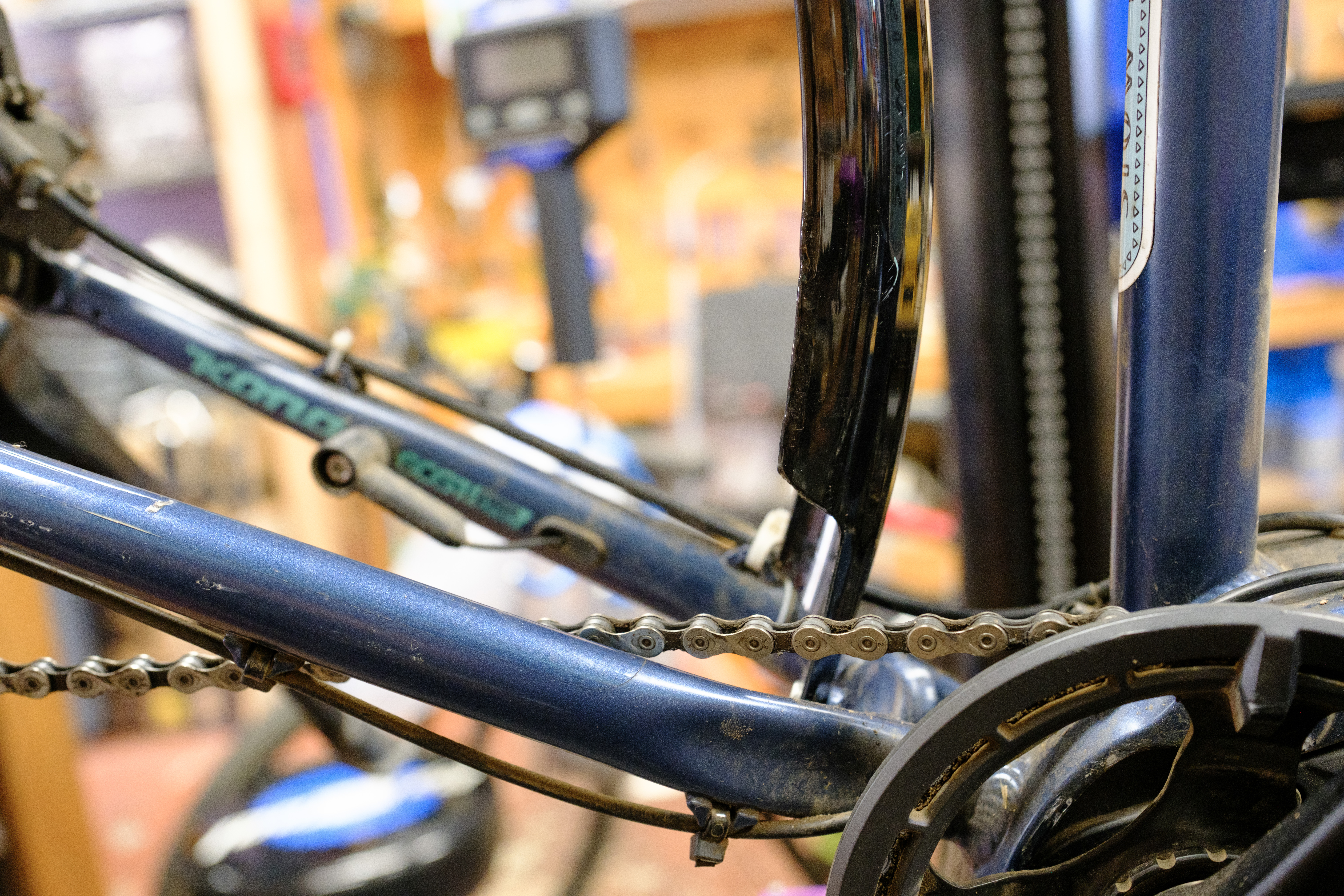 The chainstay bridge of a blue bike with the rear wheel removed showing just the black fender being setup. The bottom edge of the fender is slightly warped