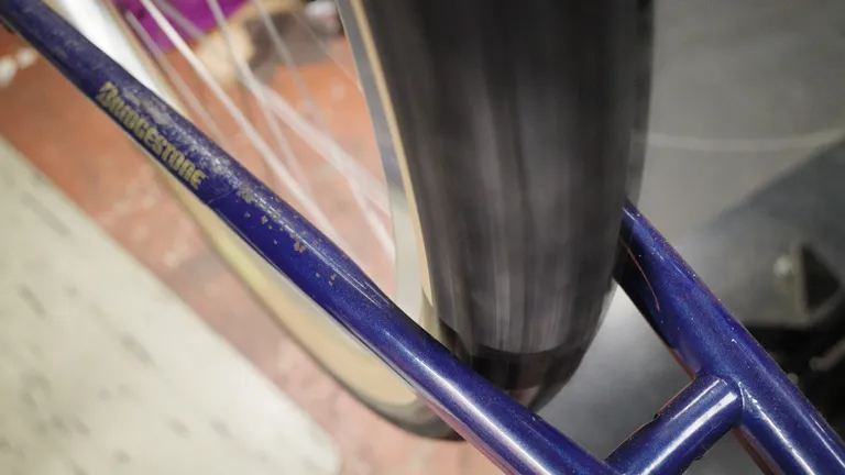 A spinning tire between two blue chainstays. The chainstay in front says "Bridgestone"