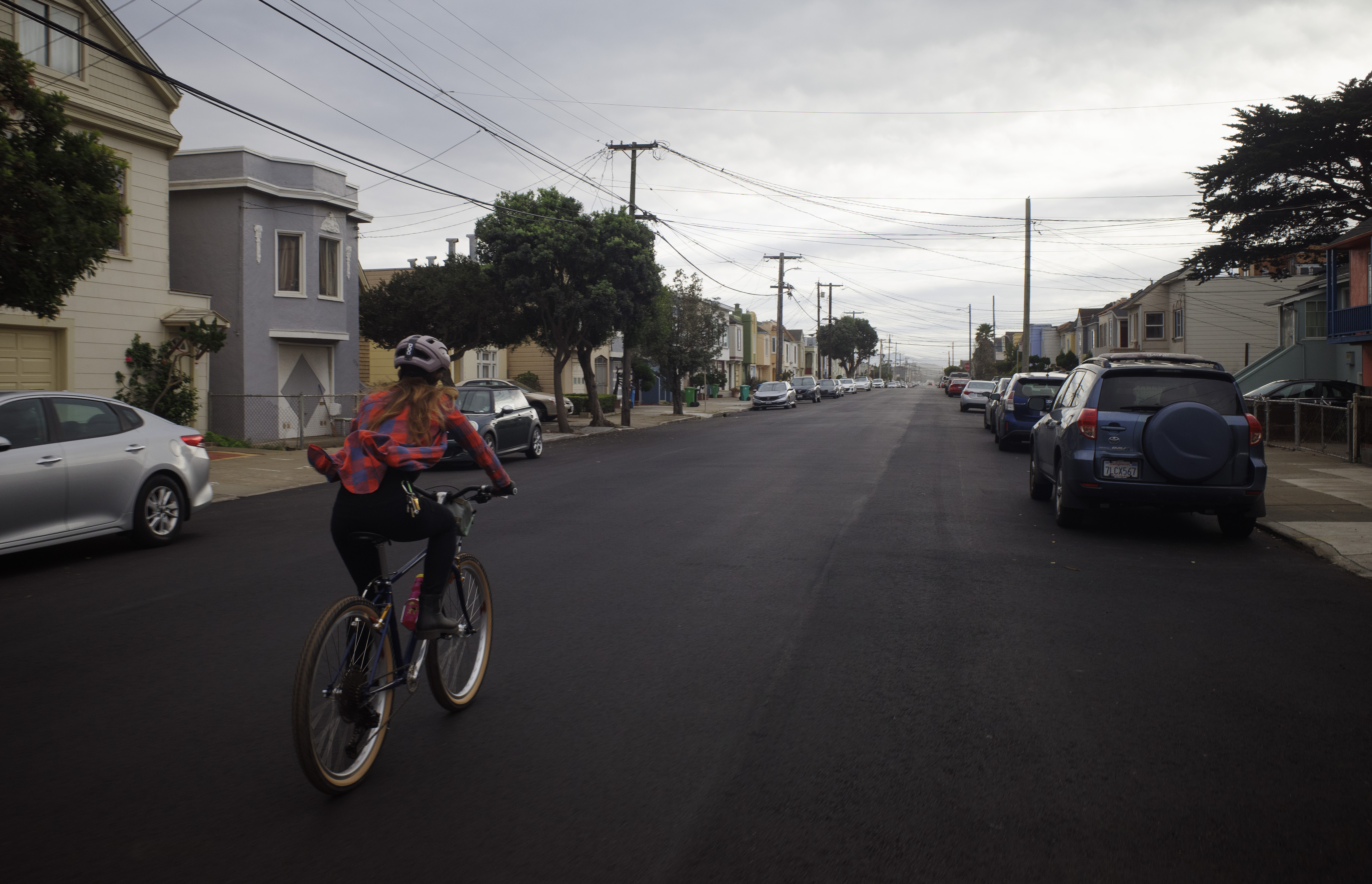 Kat on her bike on a smoothly paved road with dramatic clouds in the background. Her flannel is flapping in the wind.