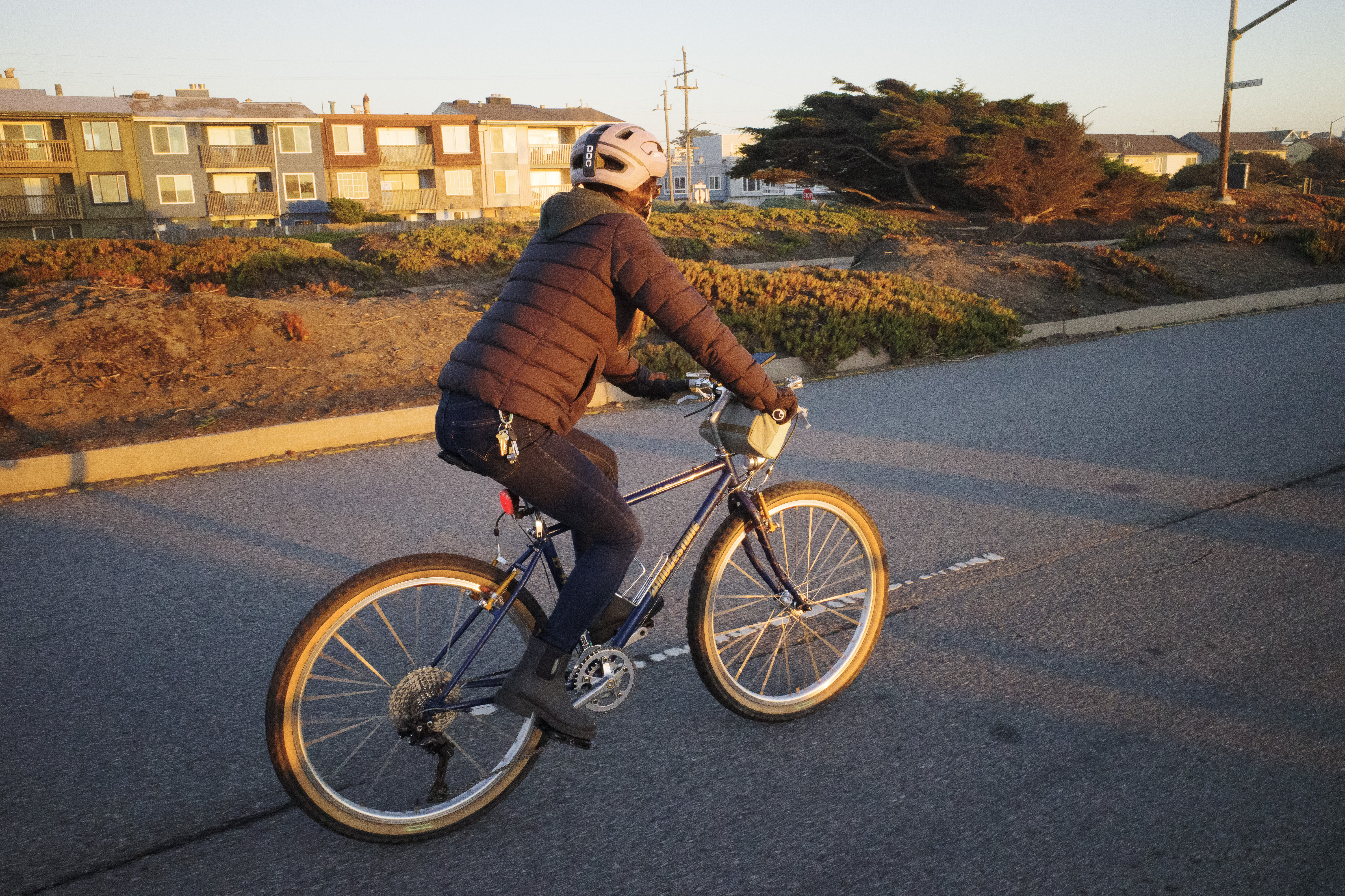 Kat riding a blue bike with gold accents on a road during golden hour.
