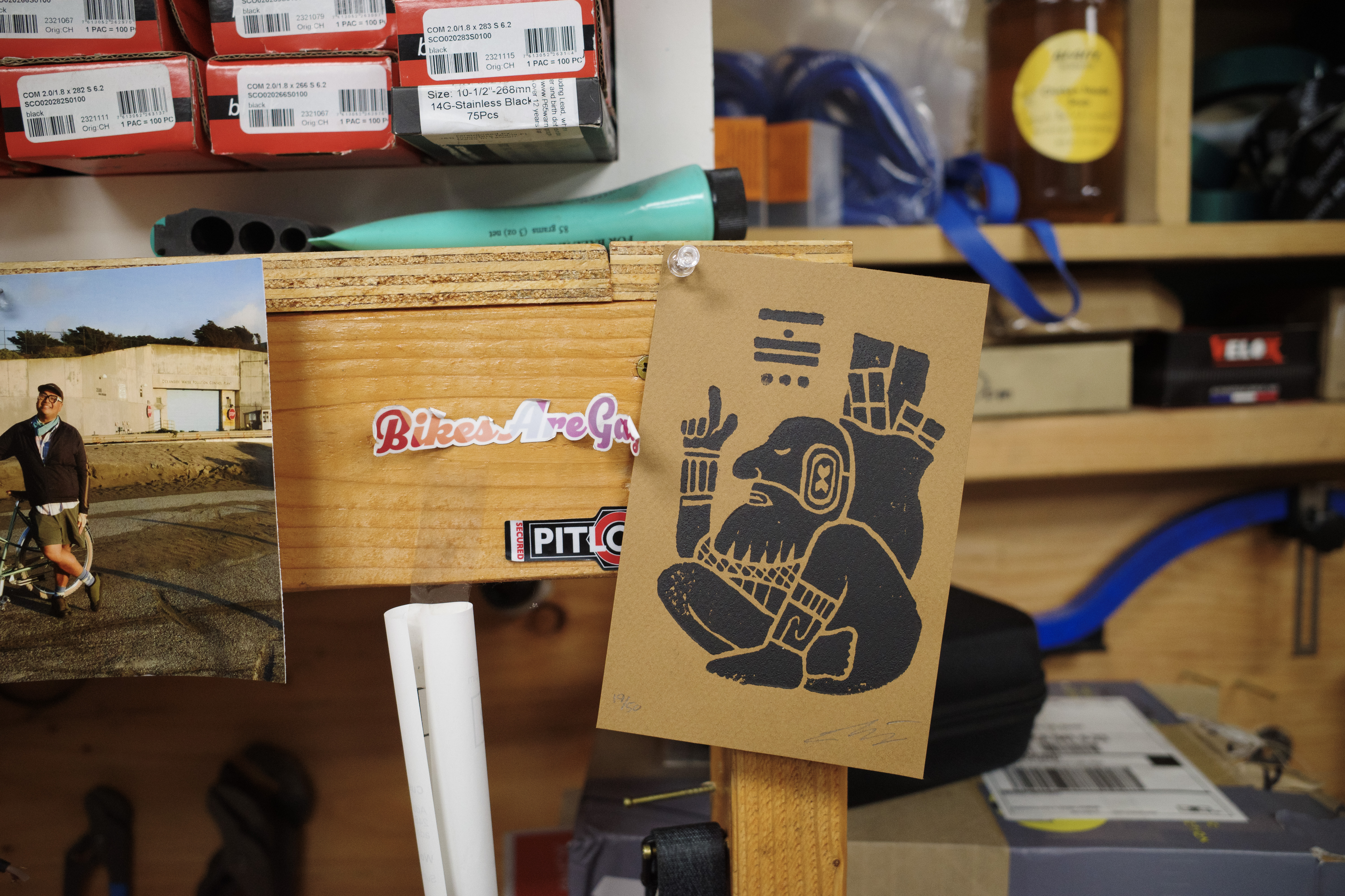 A black wood block print thumb tacked to a bench in a bike shop.
