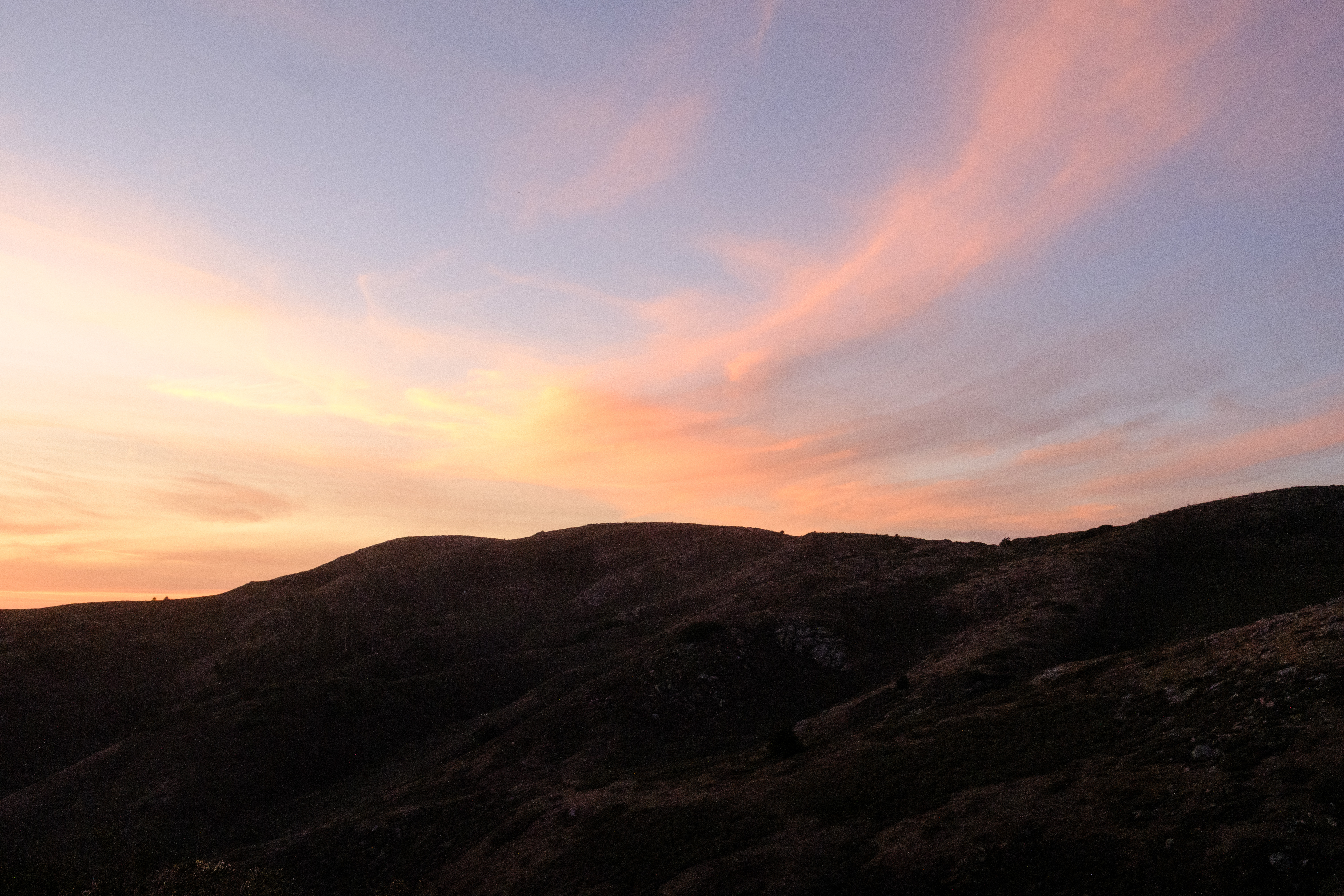 A reddish orange sunset behind the hills with swooping clouds