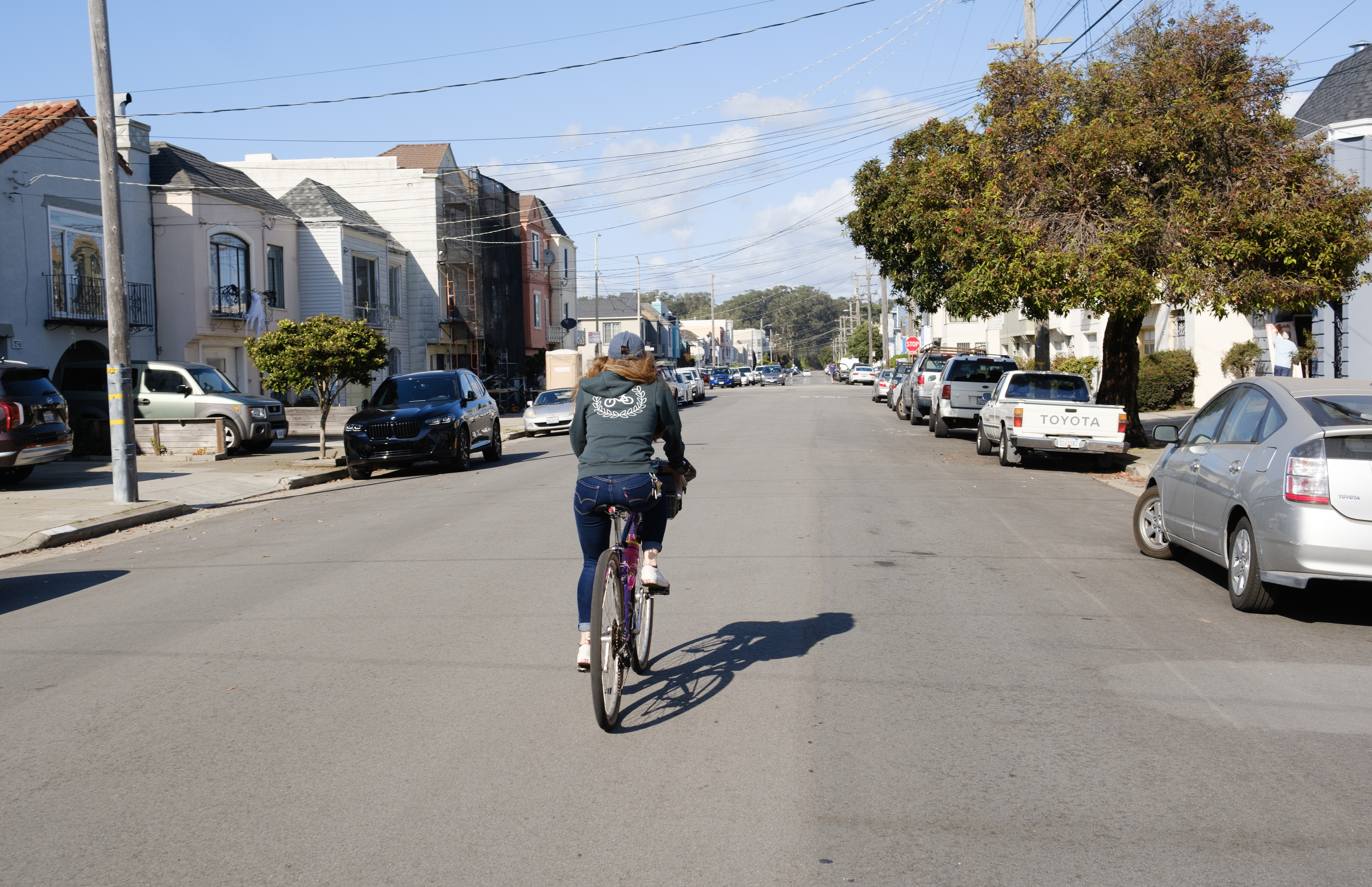 Kat in a green sweater riding down a street with a blue sky and clouds.