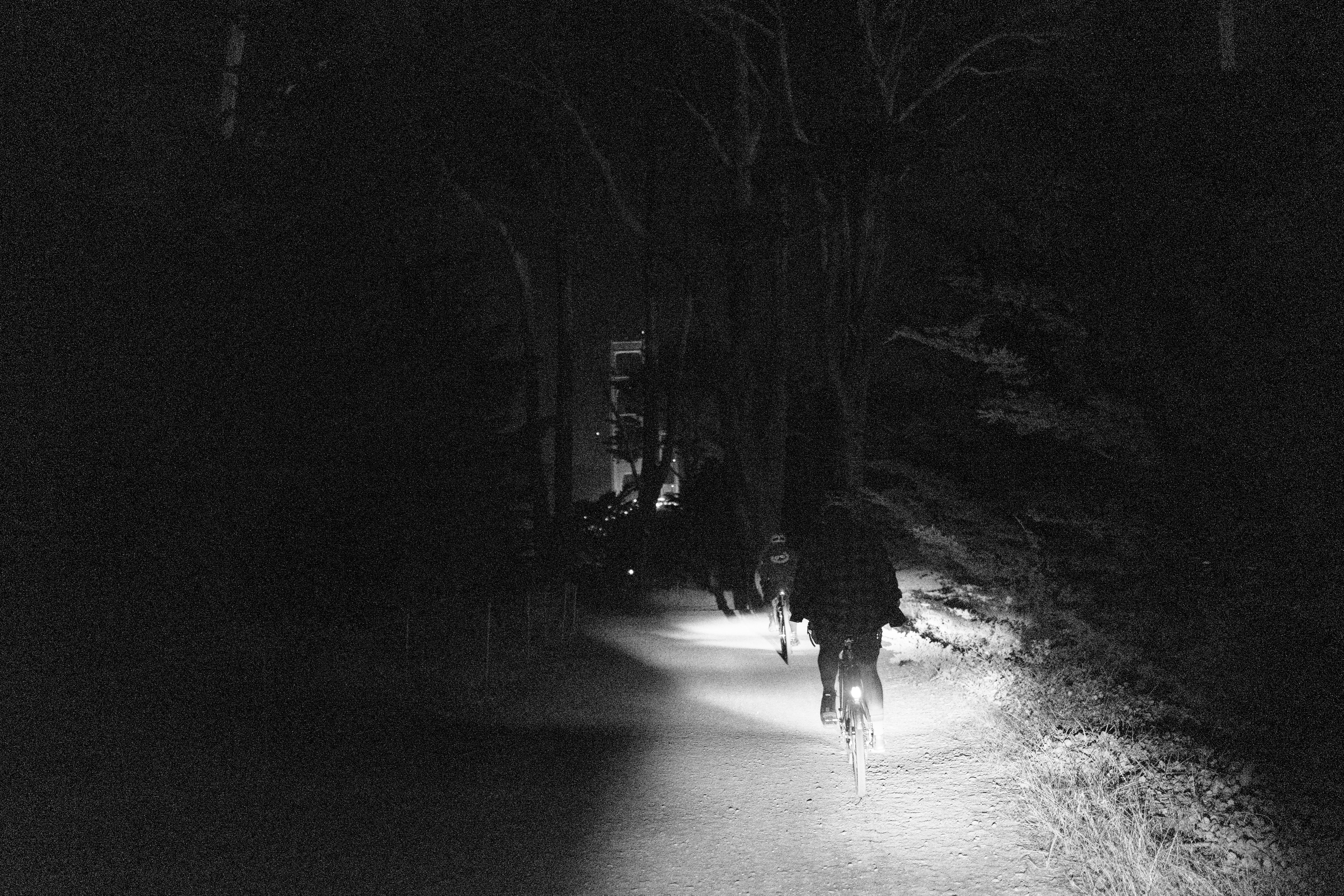 Jerry and Kat riding on a dirt trail in the dark with their headlamps on, riding towards the Golden Gate Bridge (slightly visible)