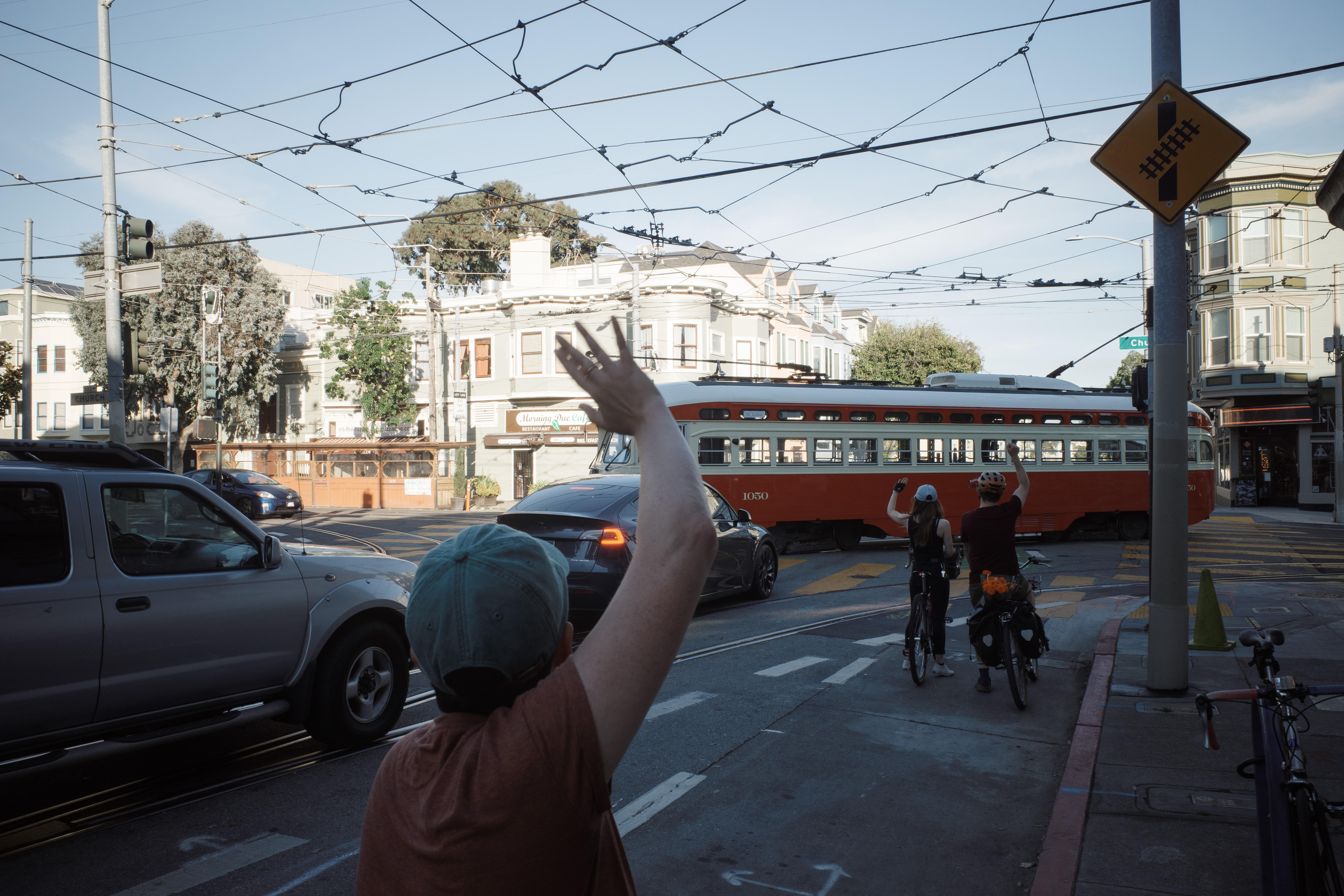 Three people on bikes waving at historic streetcar #1050.