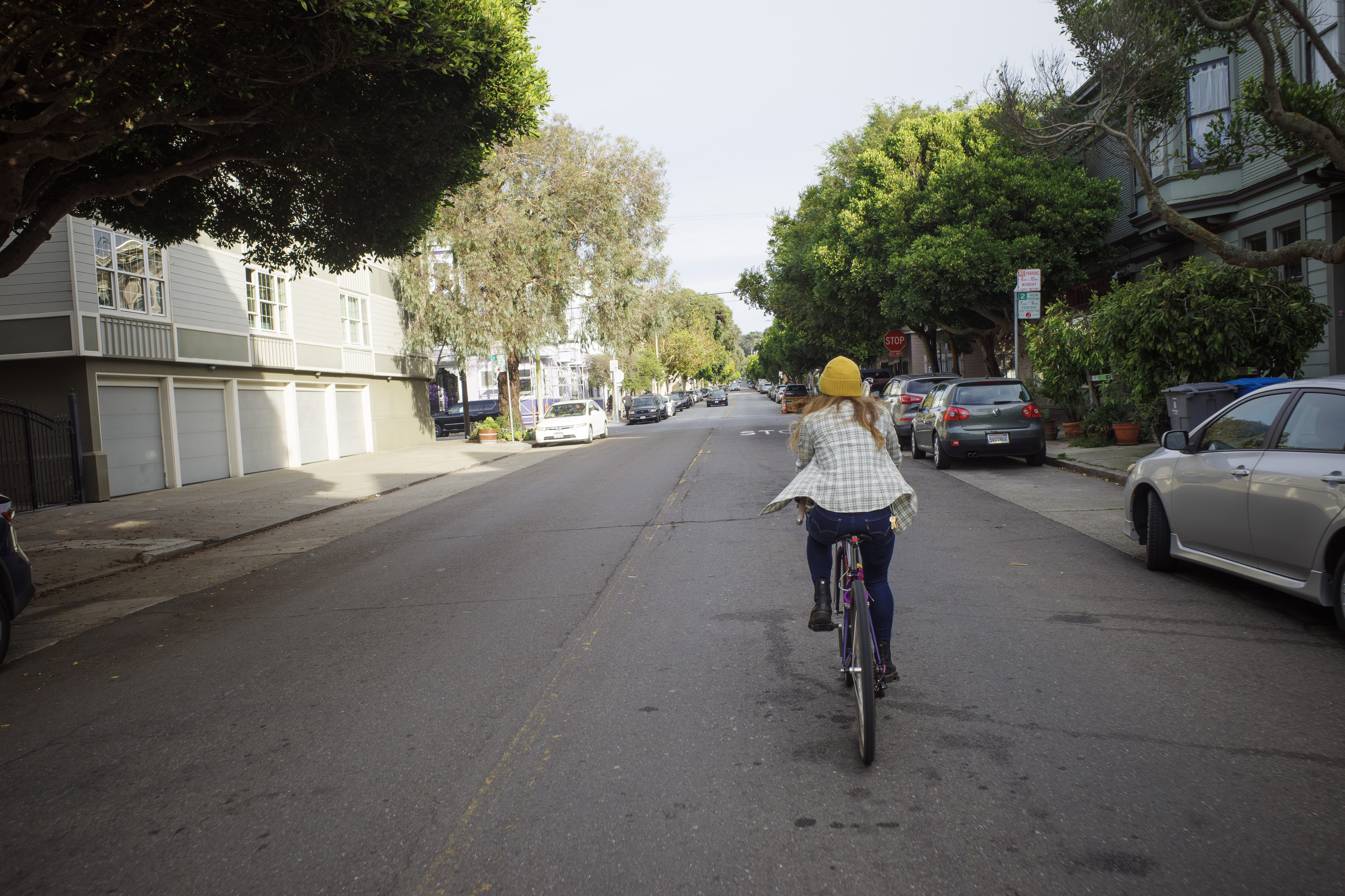 Kat riding down Waller St under some sidewalk trees with her flannel blowing in the wind