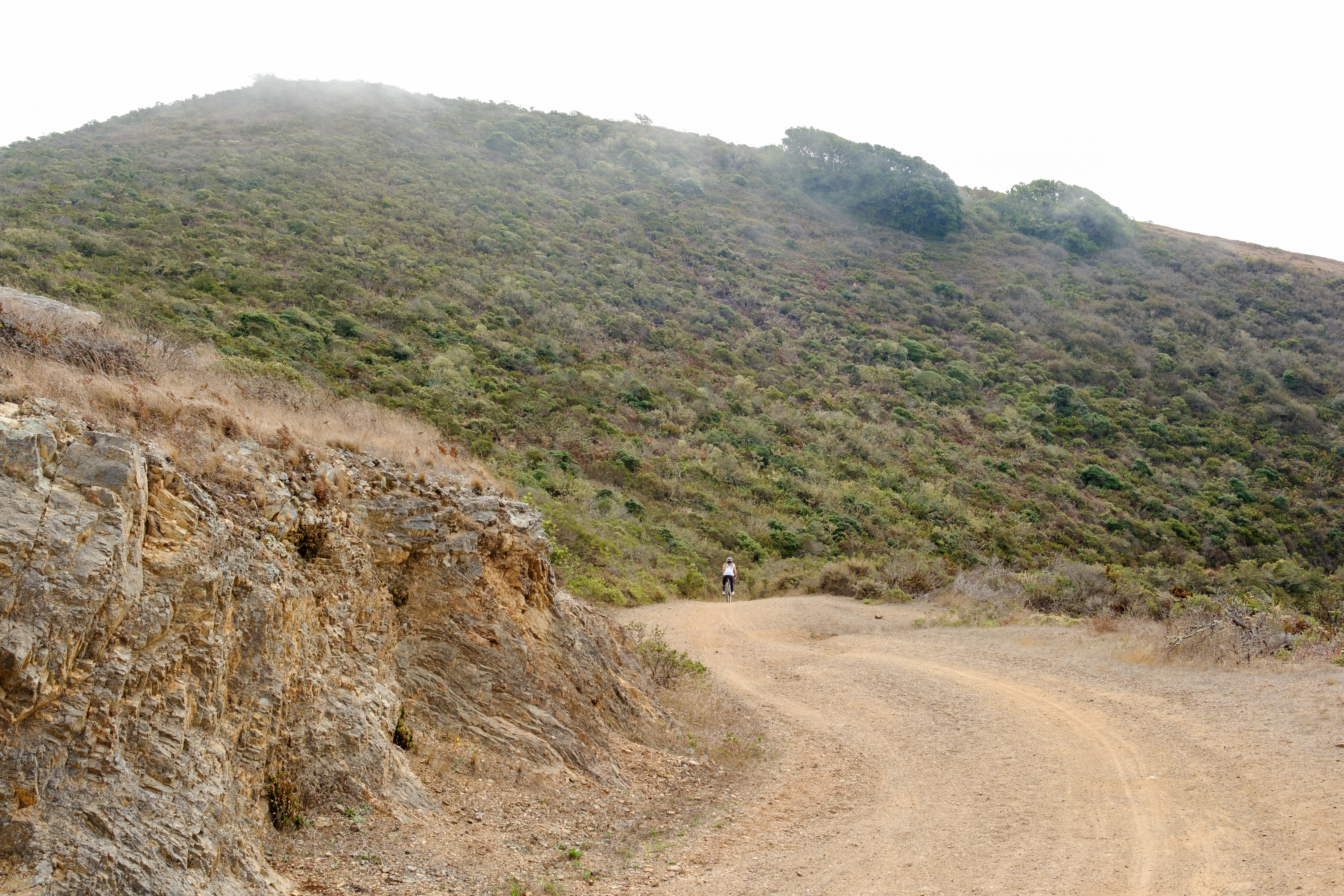 Kat descending a twisty bit of the gravel Julian trail. Fog is coming down the hill in the background.