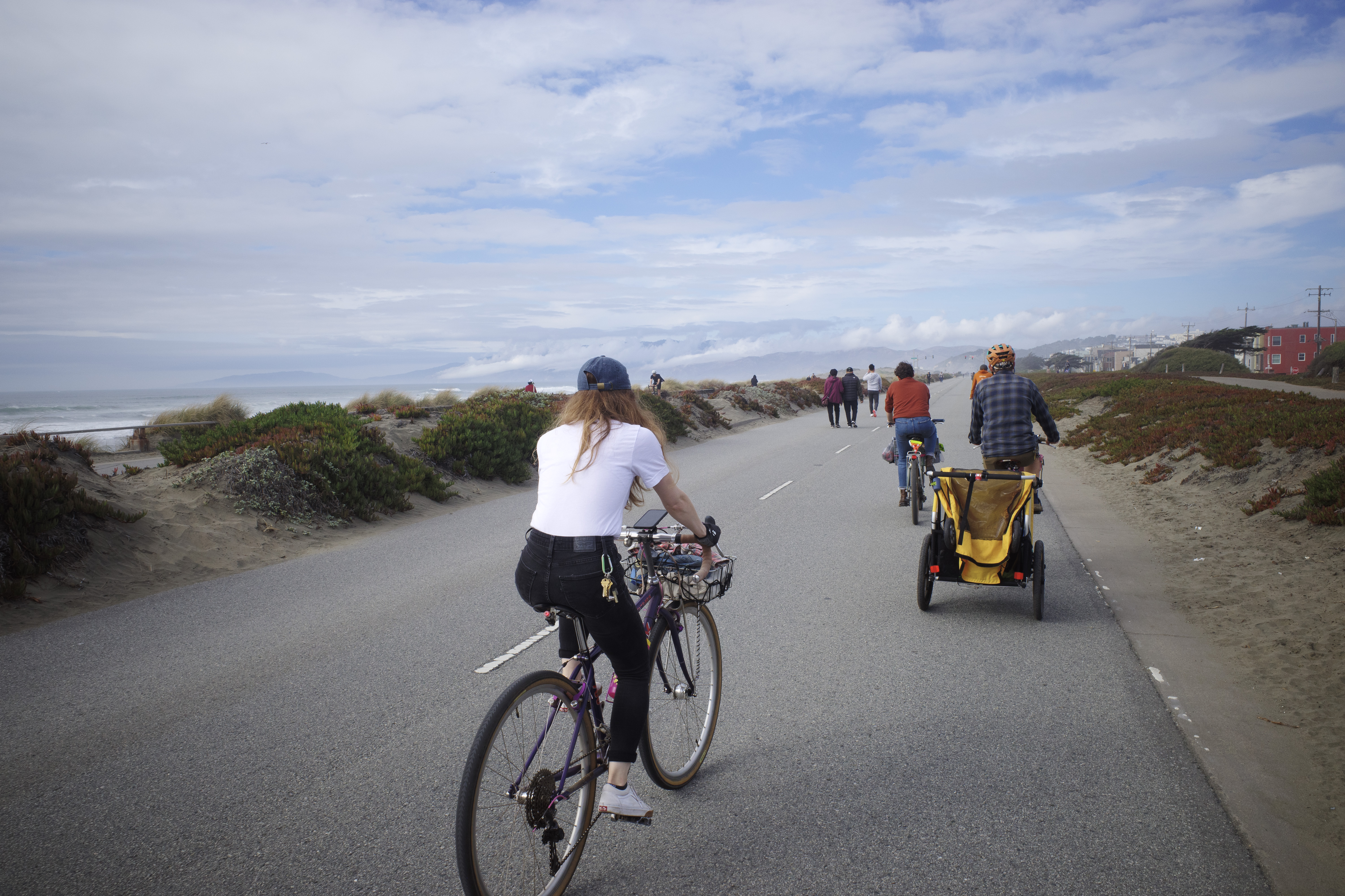 Kat, Jerry, and Sarah riding northbound on the Great Highway facing the headlands with a blue sky and lots of broken up clouds