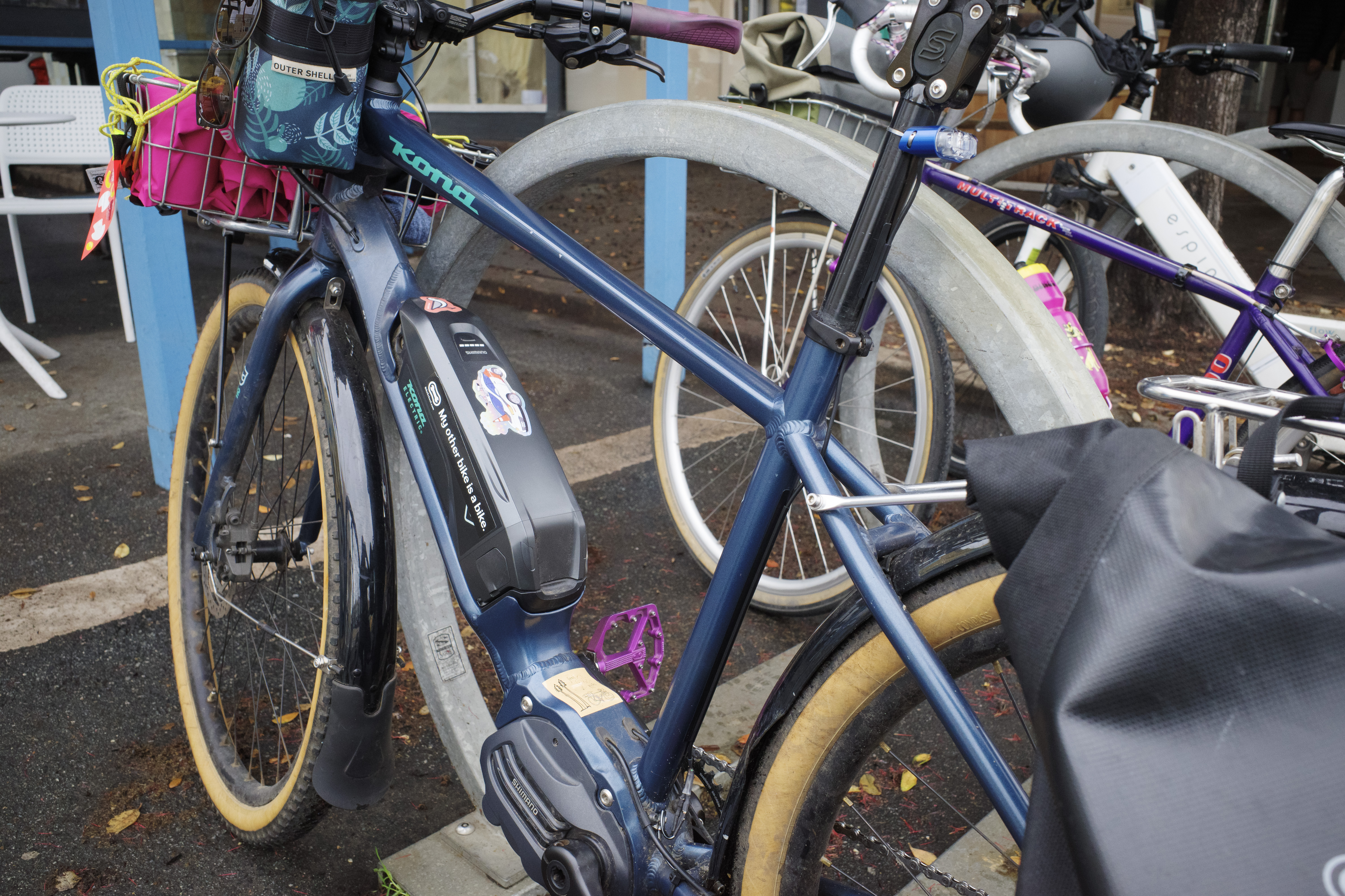 A blue e-bike against a bike rack with a black cable guide on the seat tube and seatpost.