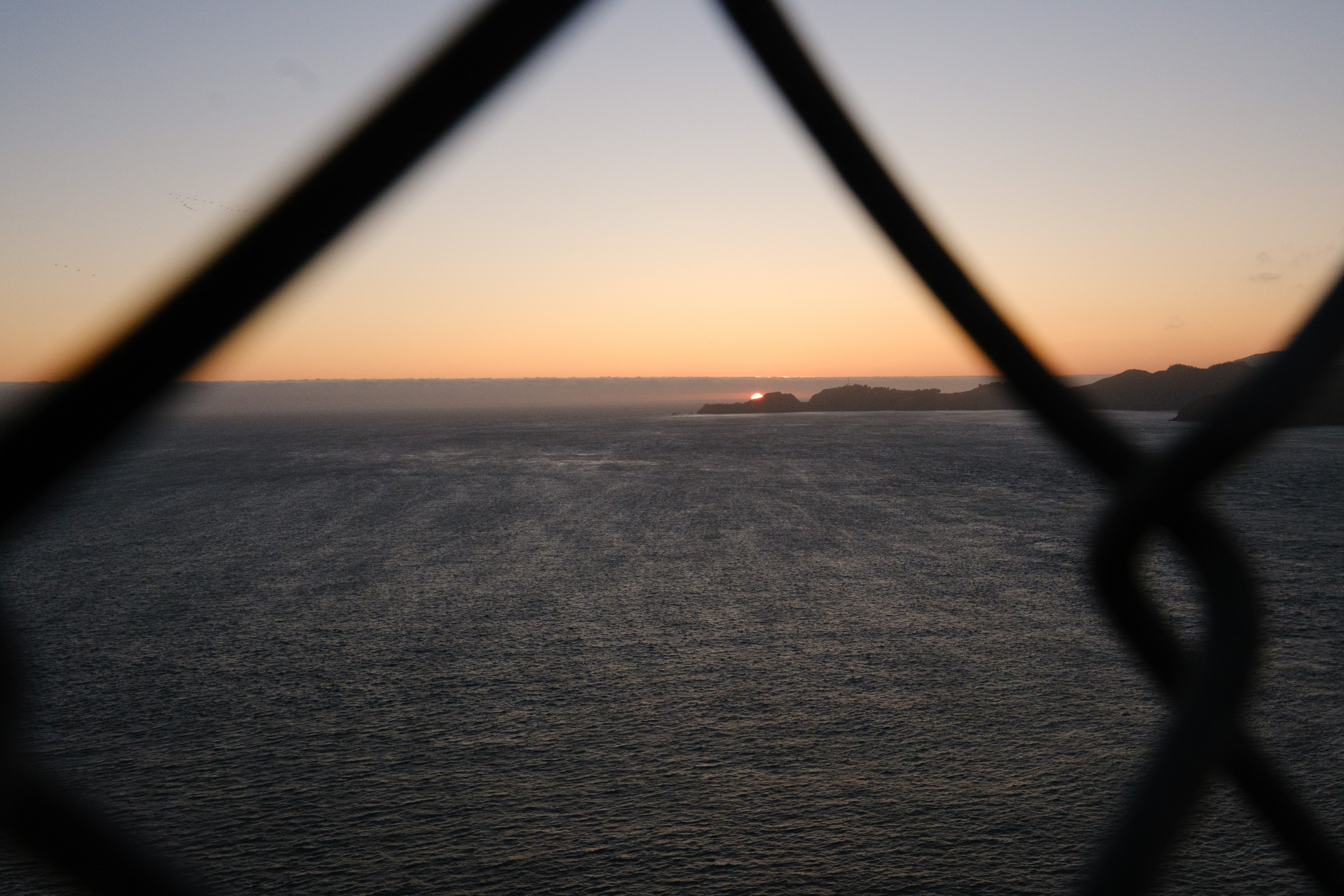 A sun almost below the horizon behind a large view of the Pacific ocean