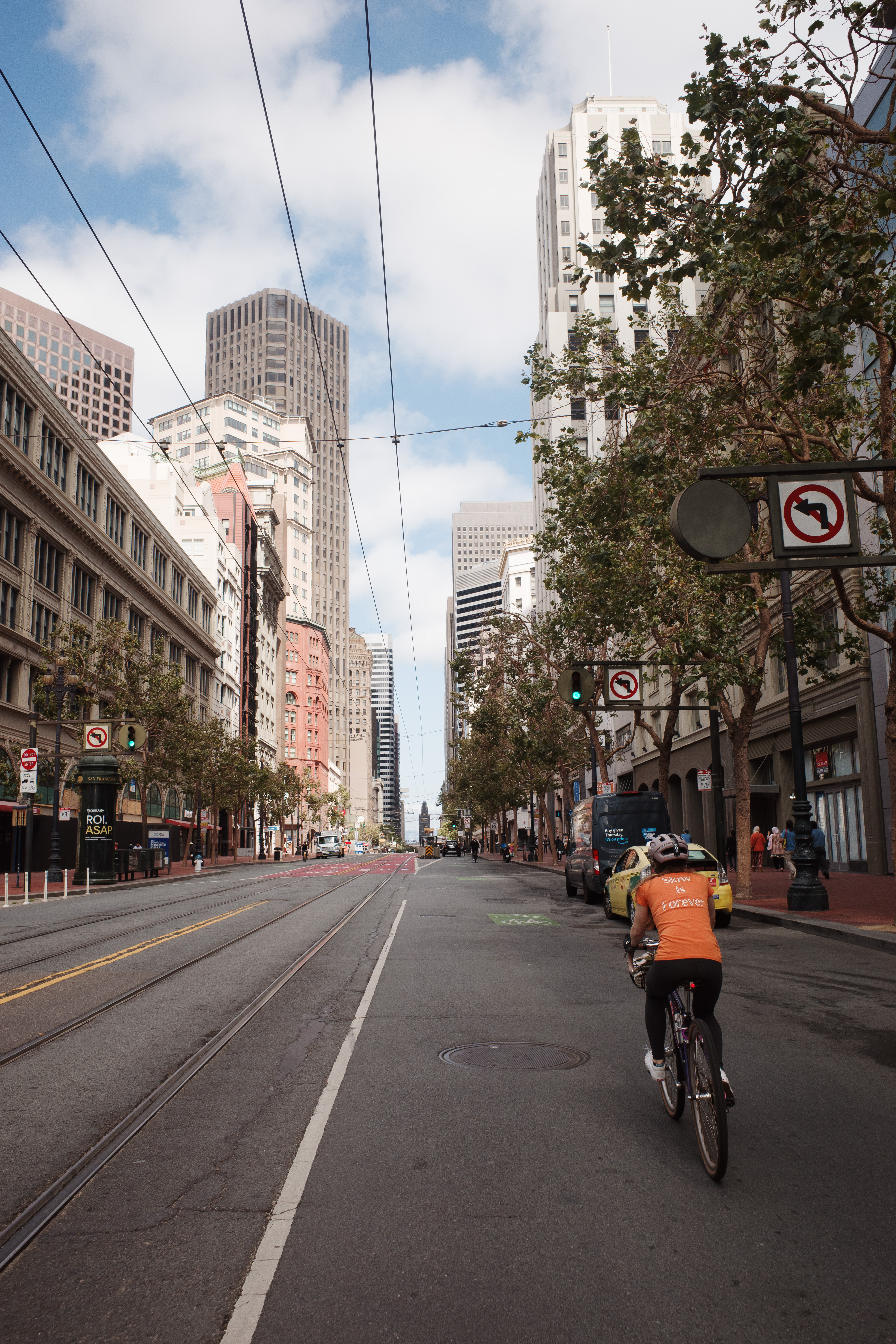 A woman in an orange 'Slow is Forever' shirt riding in a downtown street with the ferry building in the background