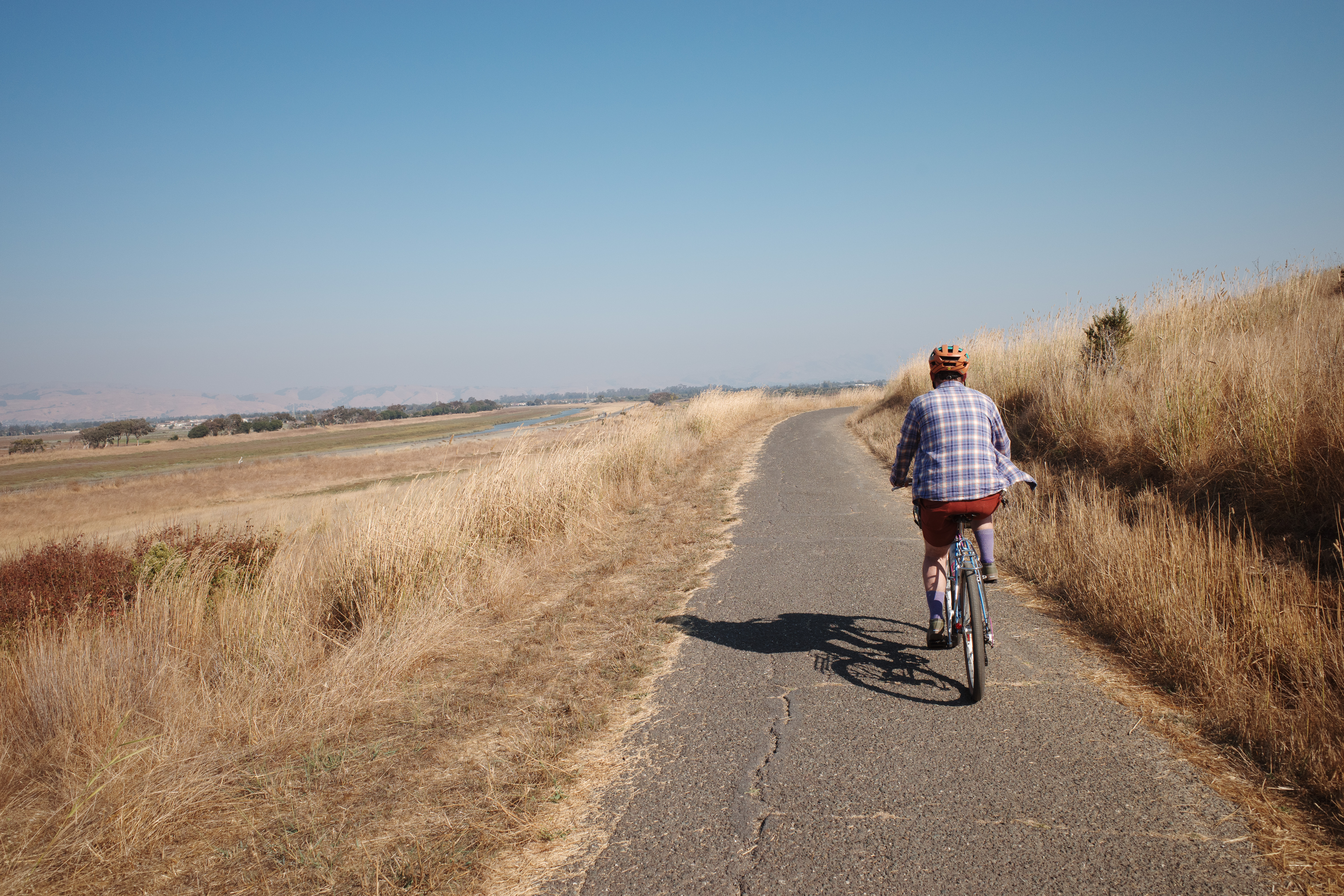 A rider wearing flannel biking through a paved path with grass on each side