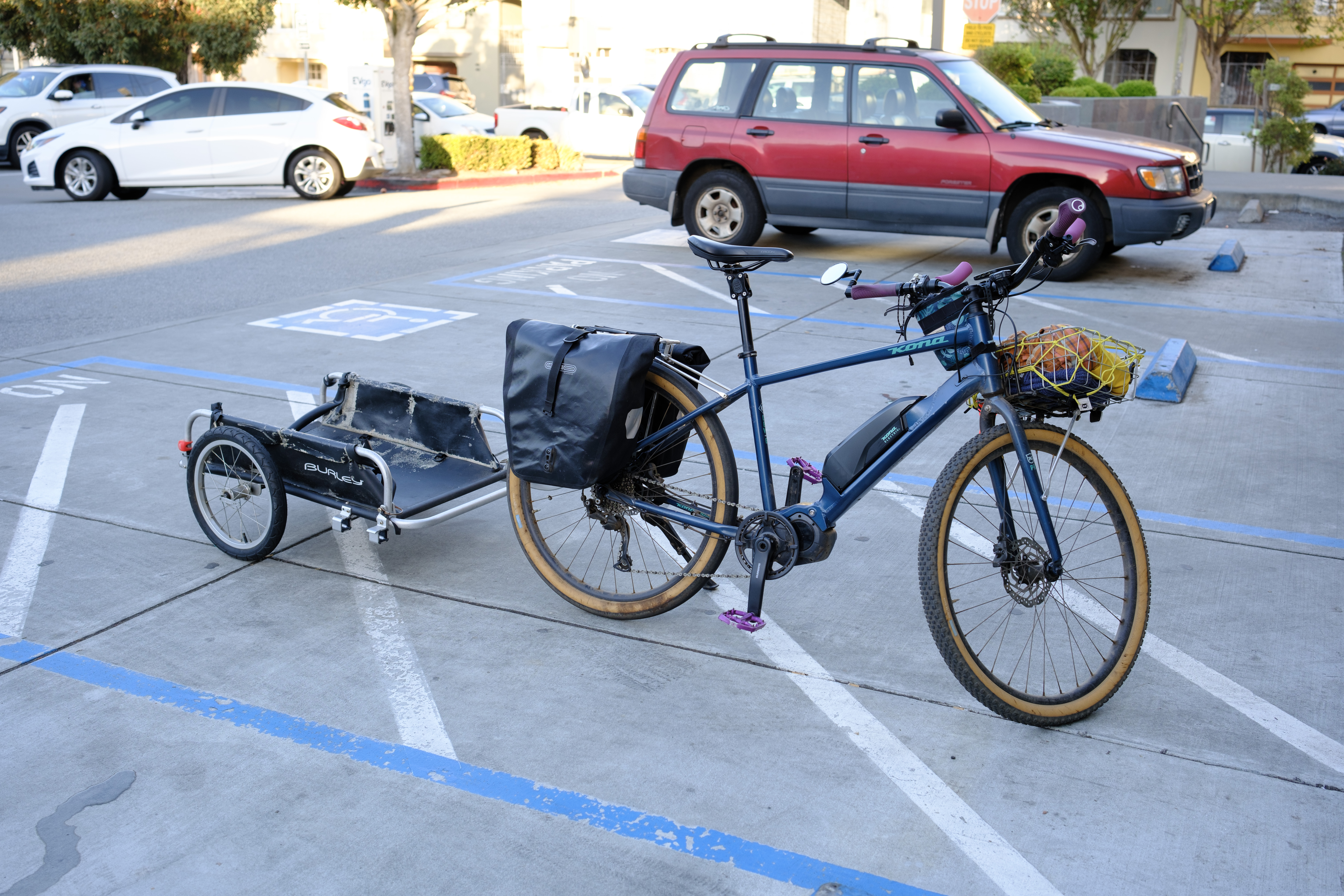 A blue e-bike in a parking space with a Burley trailer hitched to its back