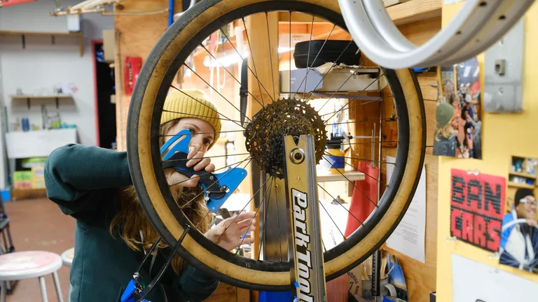 A wheel in a truing stand with a person standing behind it with a tension meter.